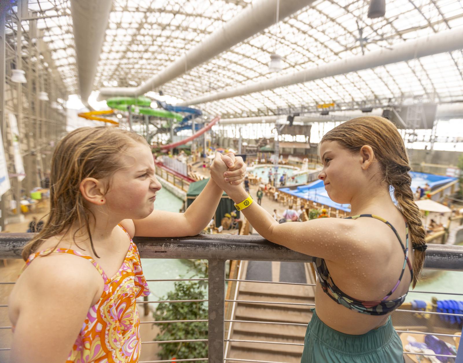 Two girls in swimsuits arm wrestling at an indoor water park.