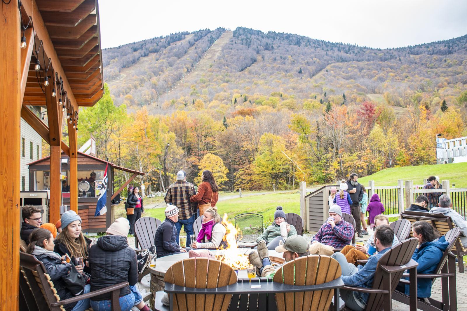 People relaxing on a patio, autumn trees and mountains in the background.